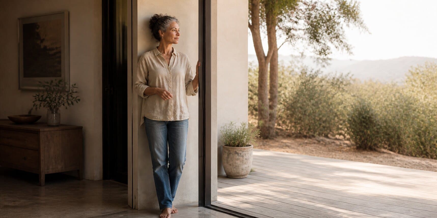 A woman over 50 standing at the threshold of a sunlit space and reflecting on her next chapter