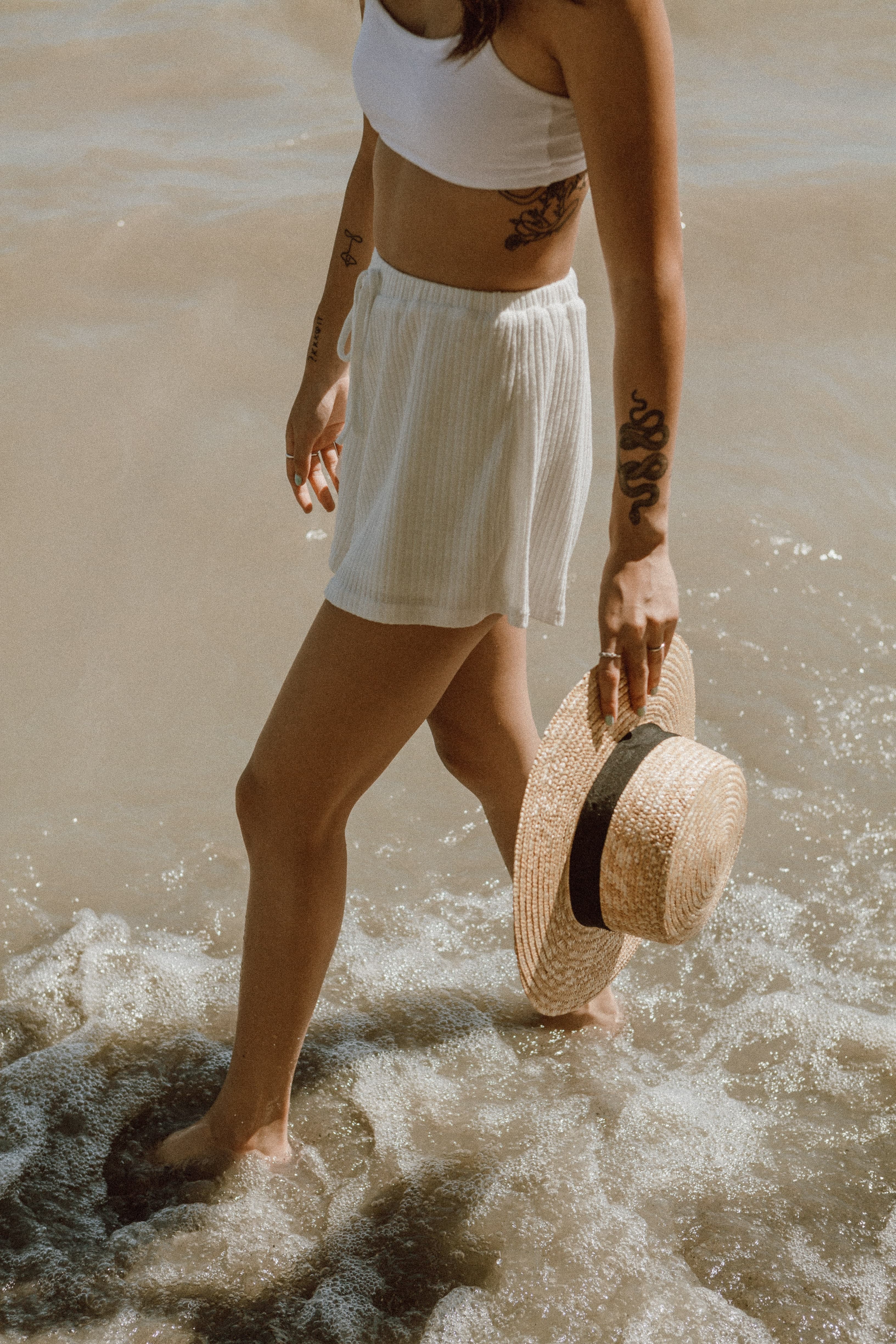 Woman walking at the shoreline while holding a wide-brimmed hat