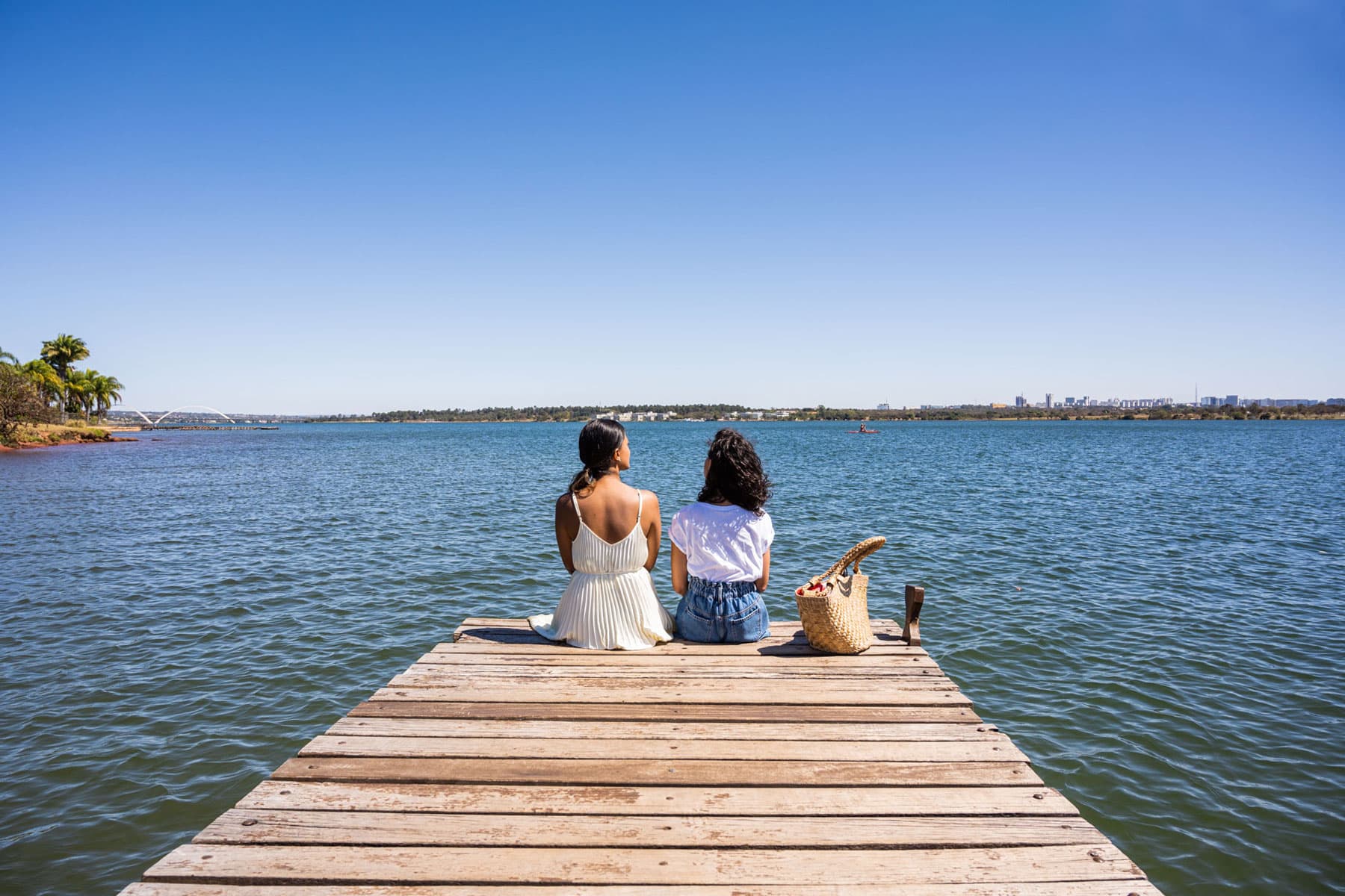 Two women sitting together at the end of a wooden dock overlooking the water